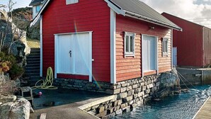 A red wooden house with a stone foundation, white garage doors, and a small porch. - 6 Person Holiday Home in Austrheim (Austrheim)