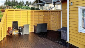 A wooden deck with outdoor furniture, a yellow building, and a covered area with a roof. - 6 Person Holiday Home in Austrheim (Austrheim)