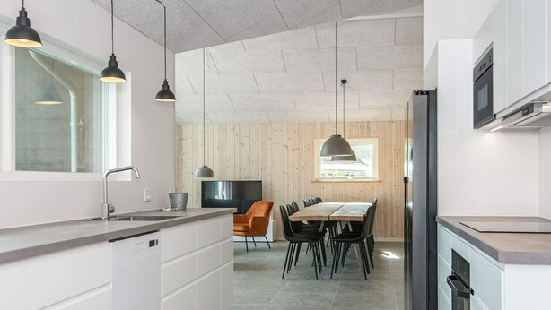 A modern kitchen with white cabinetry, a large island, pendant lighting, and a dining area with a table and chairs. - Holiday Home in Glesborg (Glesborg)