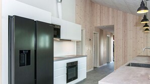 A modern kitchen with a black refrigerator, white cabinetry, and a wooden accent wall. - Holiday Home in Glesborg (Glesborg)