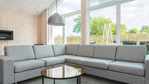 A modern living room with a grey sectional sofa, a round glass coffee table, and a mounted TV on a wooden wall. - Holiday Home in Glesborg (Glesborg)