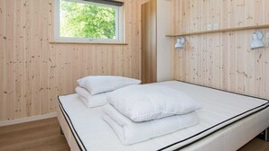 A room with wooden walls, a bed with white bedding, a window, and two wall-mounted lamps. - Holiday Home in Glesborg (Glesborg)