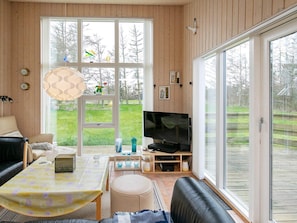 A living room with a sofa, a coffee table, a TV, and a large window with a view of a grassy yard.