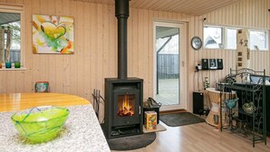 Een knus vertrek met een houtkachel, een eettafel en een groene kom op het aanrecht.