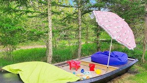 Een boot met een groene kap, een blauwe loungestoel en een roze parasol in een grasrijke omgeving met bomen.