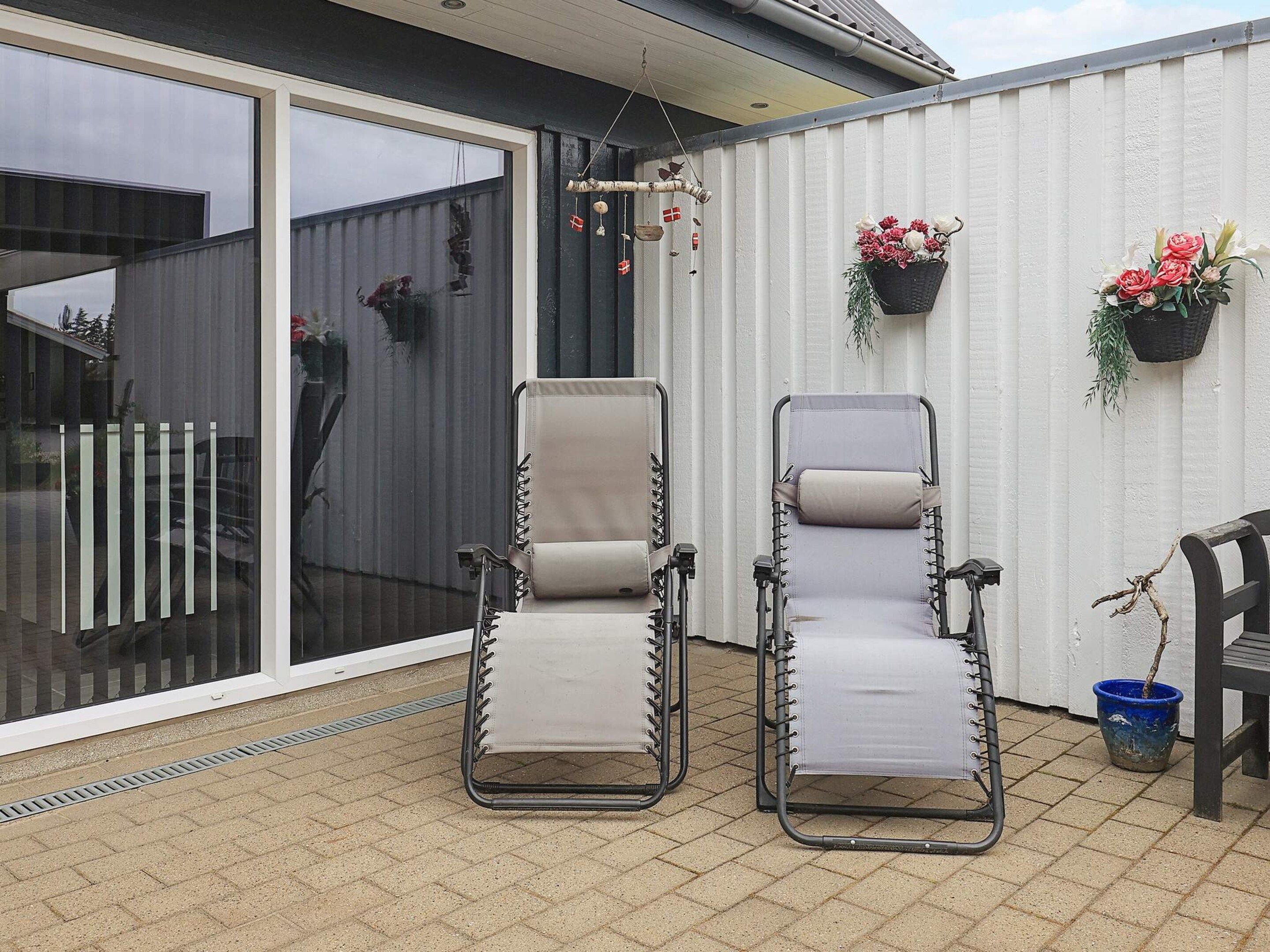 Two reclining chairs with a view of a sliding glass door and a white wall with hanging flower baskets.