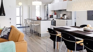 A modern kitchen with a central island, bar stools, and a dining table with chairs.