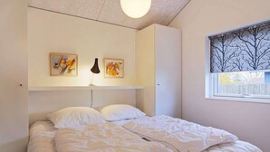 A neatly made bed with a quilted white duvet, a bedside lamp, and two framed artworks on the wall.