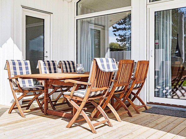 A wooden deck with a table and chairs, large glass doors, and a view of the outdoors.