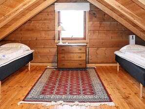 A small, cozy attic bedroom with wooden walls, a single window, a wooden dresser, two beds, and a patterned rug. - 5 Person Holiday Home in Vassenden (Sunnfjord)