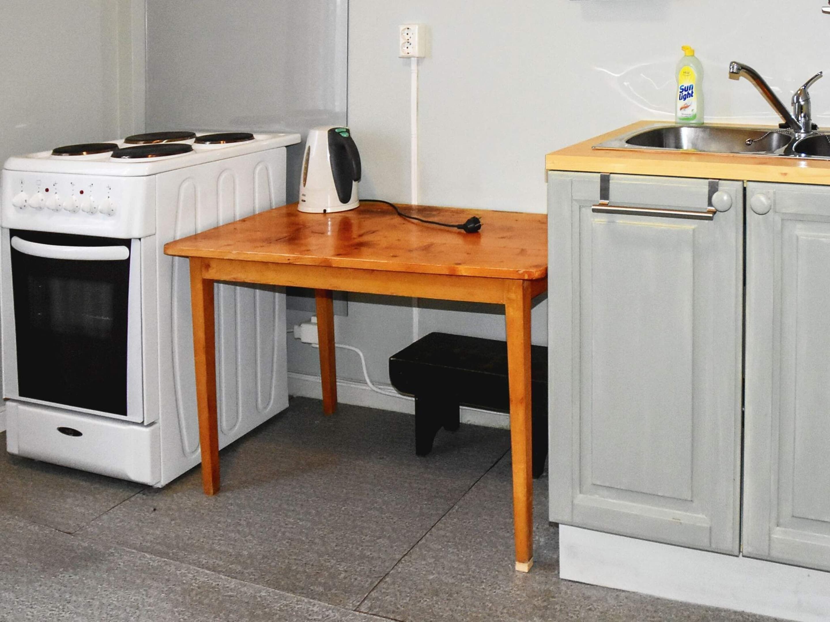A compact kitchen with a white stove, a wooden table, and a grey cabinet.