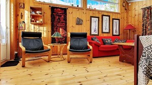 Een knus vertrek met houten wanden, een rode bank, twee stoelen, een kleine tafel en een raam met uitzicht op bomen.