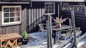 Een houten terras met een tafel, stoelen, een bloempot en een raam.