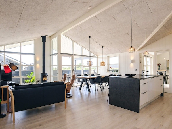 A spacious kitchen with a large island, modern pendant lights, and a view through large windows.