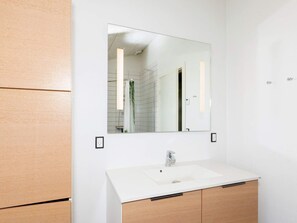 A modern bathroom with a white sink, wooden cabinets, and a large mirror. - Holiday Home in LÃ¸kken (Lokken)