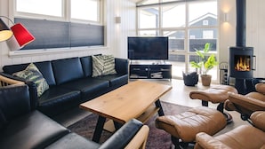A modern living room with a sofa, TV, coffee table, and fireplace. - Holiday Home in LÃ¸kken (Lokken)