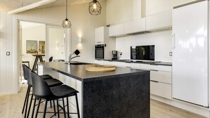 A modern kitchen with a central island, black bar stools, pendant lighting, and a white refrigerator. - Holiday Home in LÃ¸kken (Lokken)