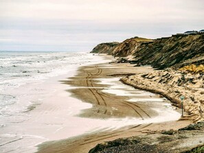 A coastal beach with a sandy shoreline, cliffs, and a clear view of the ocean.