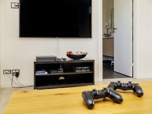 A room with a television mounted on the wall, a wooden table with a game controller, and a black entertainment unit with electronic devices.