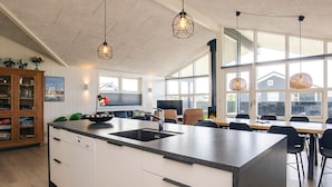 A modern kitchen with a central island, built-in appliances, and large windows offering views of the outside. - Holiday Home in LÃ¸kken (Lokken)