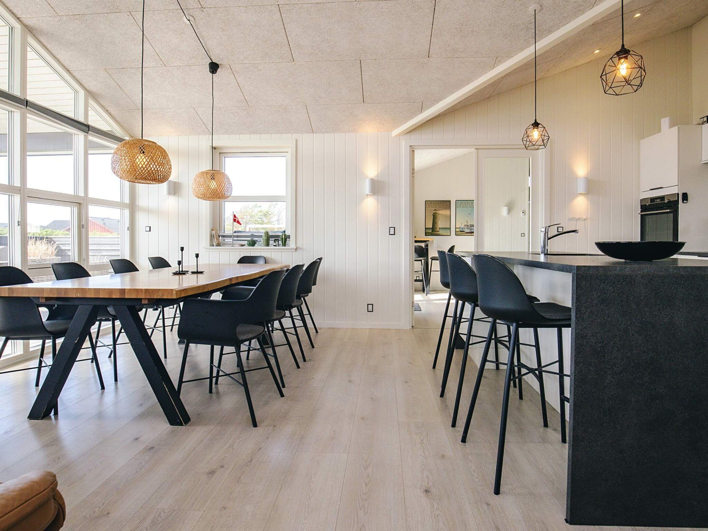 A modern kitchen with a wooden dining table, black chairs, and pendant lights.