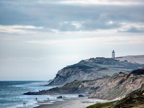 Eine Küstenlandschaft mit einem Leuchtturm auf einer Klippe, felsigem Strand und dem Ozean.