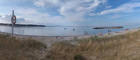A beach with a lifebuoy sign, calm water, and a distant shoreline.