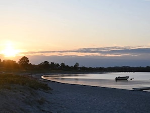 Ein Strand bei Sonnenuntergang mit einem Boot auf dem Wasser und einem sandigen Ufer.