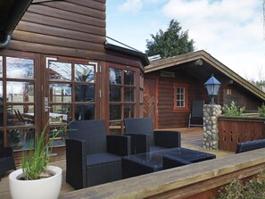 A wooden cabin with large windows, outdoor seating, and a stone pillar.