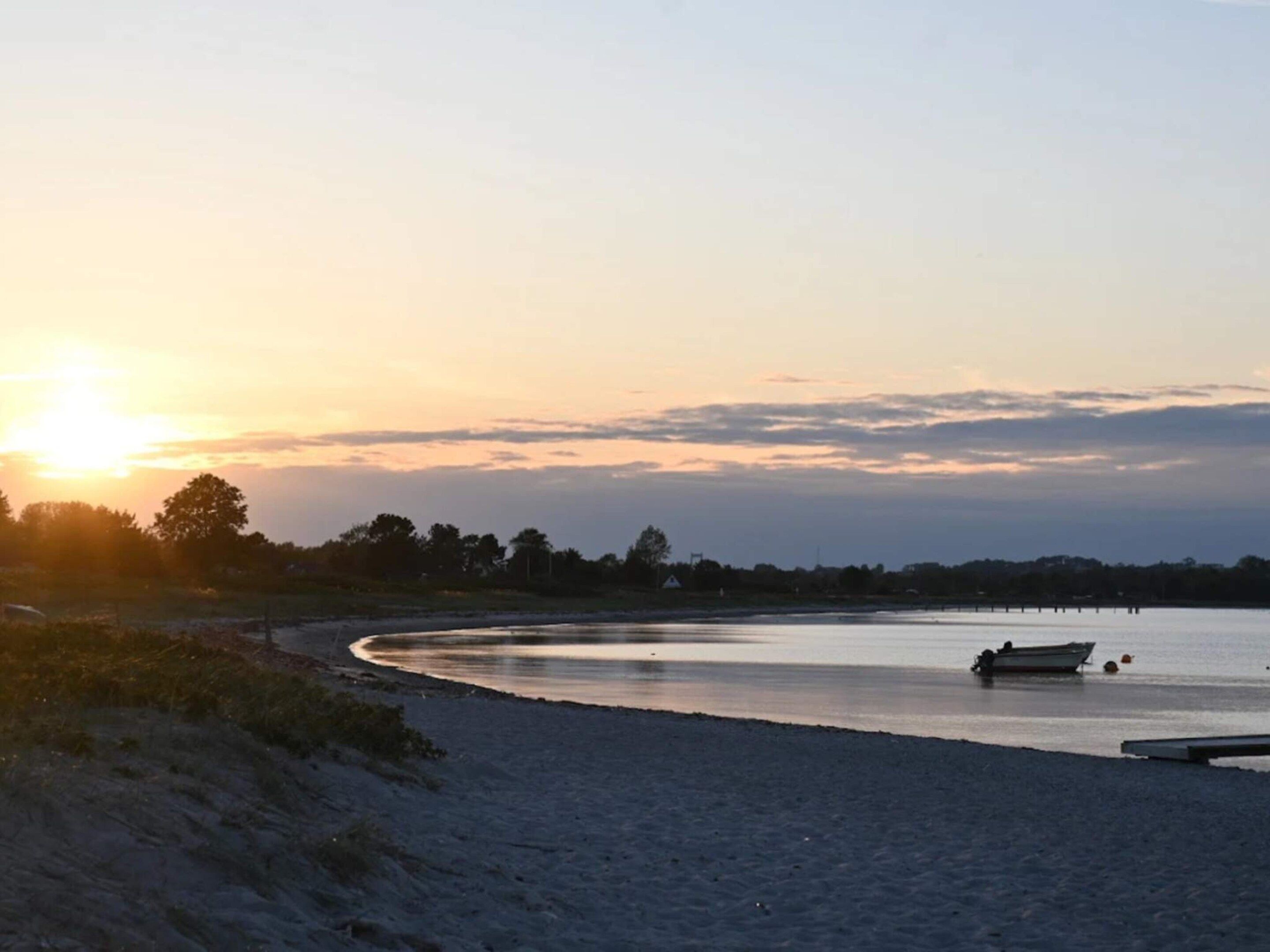 A beach with a boat on the water and a sunset in the background.