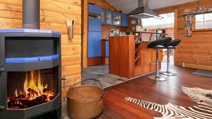 A log cabin interior with a wood-burning stove, a kitchen area, and a bar stool. - 5 Person Holiday Home in Middelfart (Middelfart)