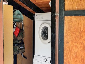 A compact laundry room with a washing machine, a drying rack, and a camouflage bag hanging on the wall.
