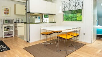 Una cocina compacta con armarios blancos, una mesa de comedor con cuatro sillas y vistas a zonas verdes por una ventana.