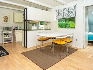 Une cuisine compacte avec des meubles blancs, une table à manger et quatre chaises, et une vue sur la verdure par une fenêtre.