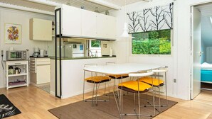 A modern kitchen with white cabinets, a built-in microwave, and a dining area with a white table and yellow chairs. - 5 Person Holiday Home in Ry (Ry)