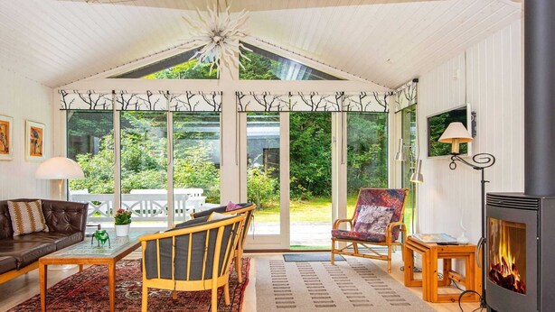 A cozy living room with a fireplace, a dining area, and large windows offering a view of the garden. - 5 Person Holiday Home in Ry (Ry)