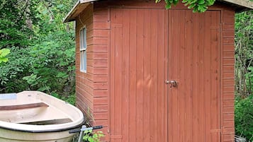 A wooden shed with a door and a window, surrounded by greenery.