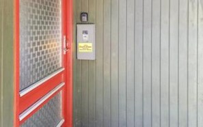 A red door with a glass panel, a metal box on the wall, and a vertical wooden paneling.