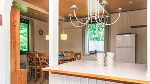 A compact kitchen with a wooden island, a dining area with chairs, a refrigerator, and a window with curtains.
