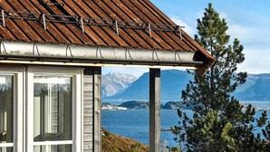 A rustic cabin with a wooden roof and large windows overlooking a coastal landscape with mountains in the background. - 6 Person Holiday Home in Kalvag (Bremanger)