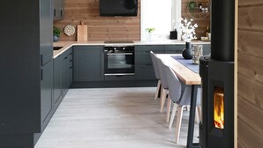 A modern kitchen with dark cabinets, a built-in oven, a black range hood, and a wood-burning stove. - 6 Person Holiday Home in Kalvag (Bremanger)