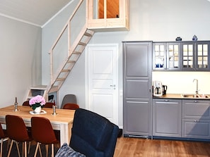 Ett kök med en trätrappa, grå skåp, ett matbord med stolar och ett litet fönster.