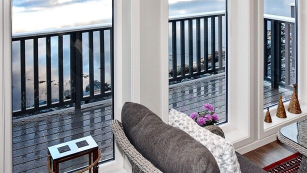 A room with large windows, a grey sofa, a small table, and a wicker chair. - 4 Star Holiday Home in Vatne (Ålesund)