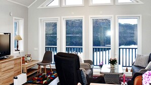 A living room with a TV, a sofa, a chair, a table, and large windows with a view of a body of water. - 4 Star Holiday Home in Vatne (Ålesund)