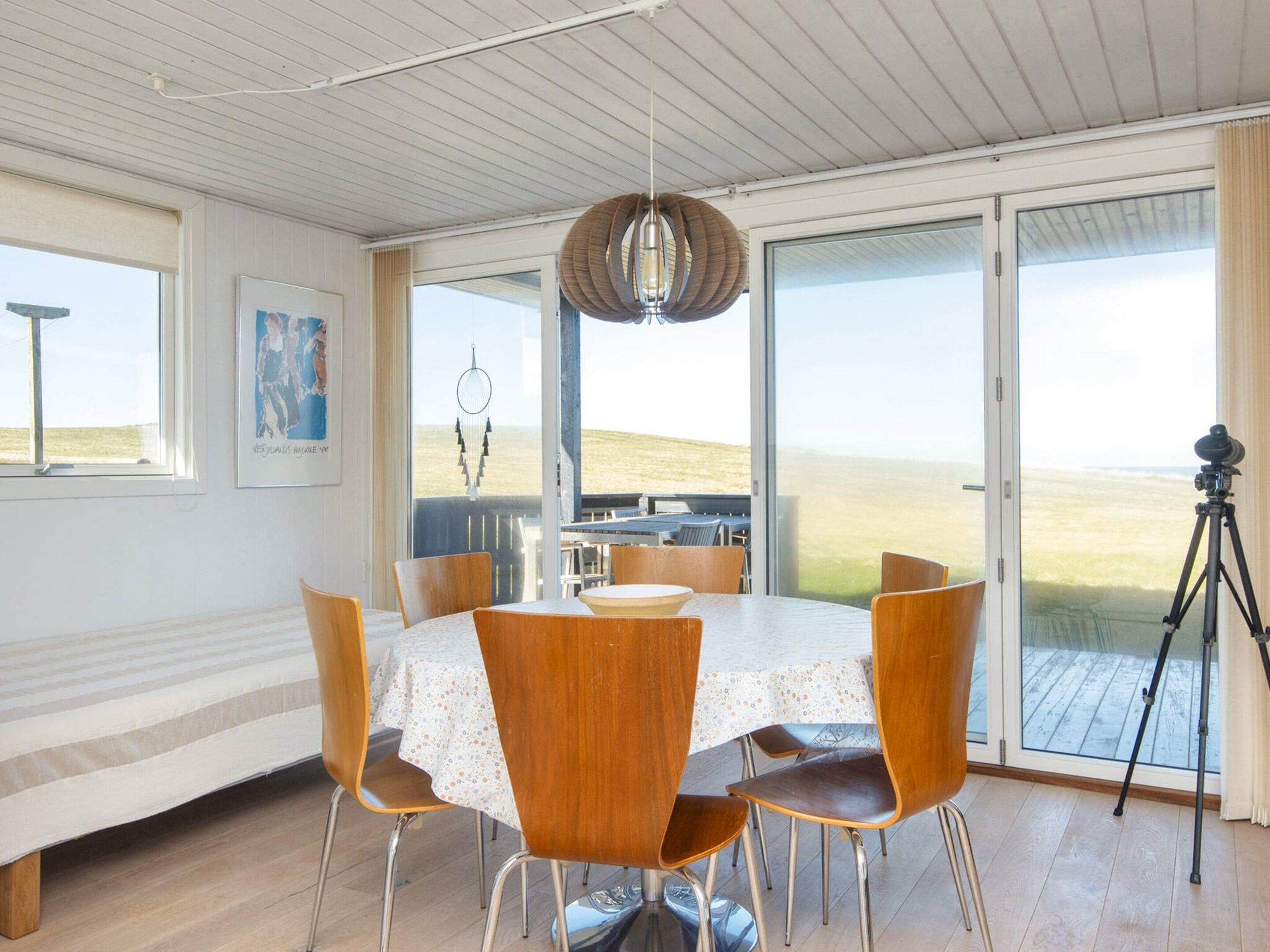 A dining area with a round table, wooden chairs, and a view through large glass doors to the outdoors.