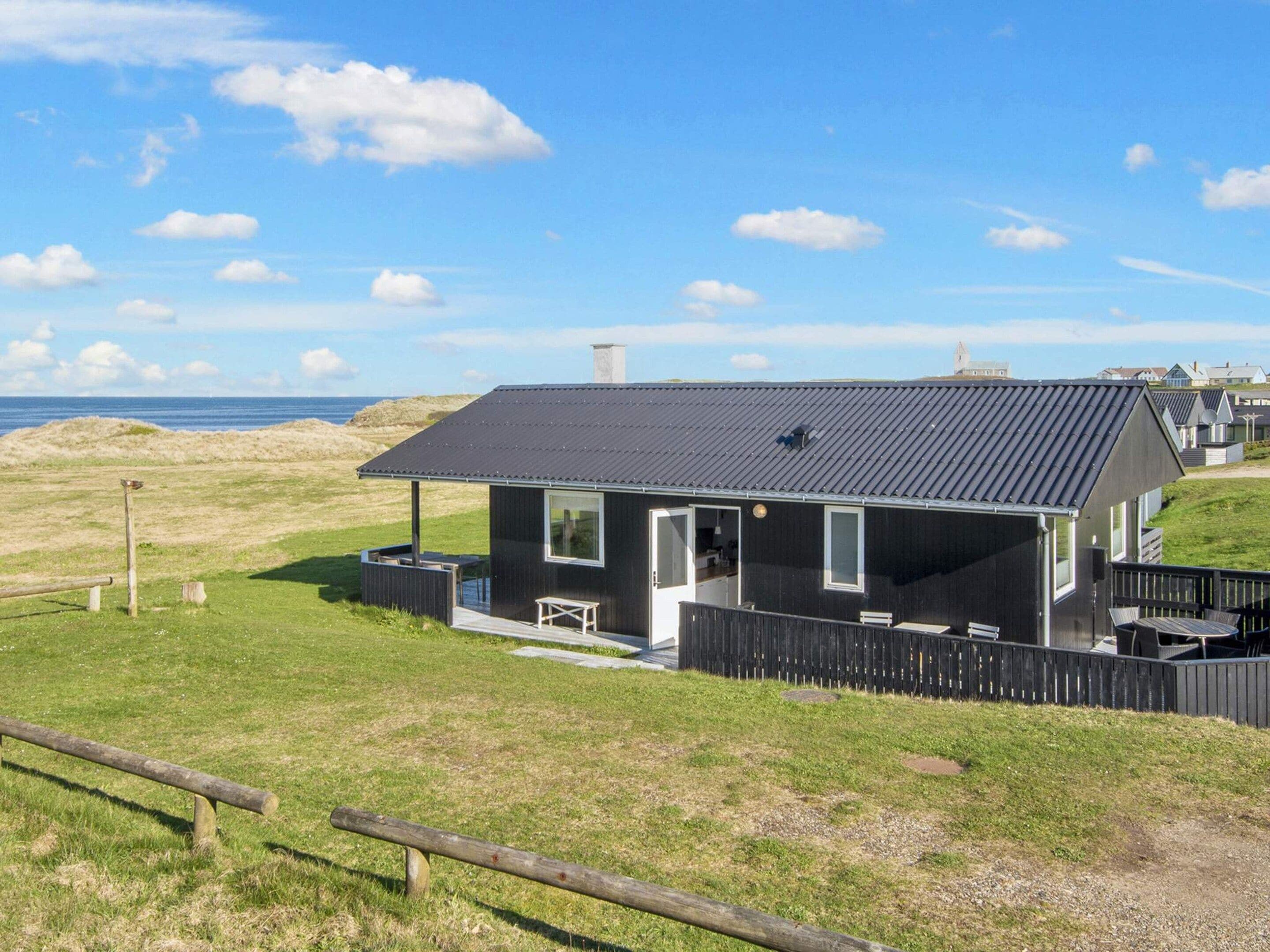 Una casa moderna negra con techo plano, una terraza y vista al mar.