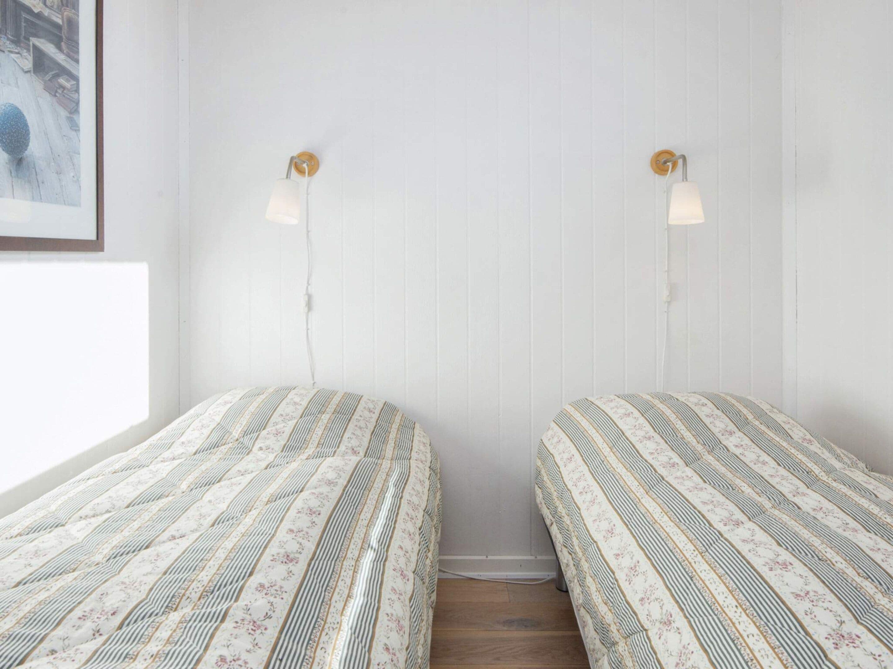 Una habitación con dos camas, cada una con colcha de rayas y motivos florales, una pared blanca y una ventana a la izquierda.