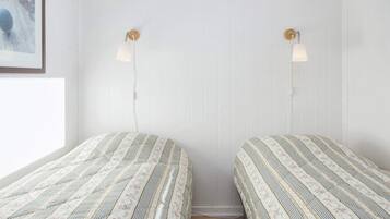 Una habitación con dos camas, cada una con colcha de rayas y motivos florales, una pared blanca y una ventana a la izquierda.