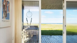 Ett sovrum med ett stort fönster och en skjutdörr i glas som leder ut till en terrass med utsikt över stranden.