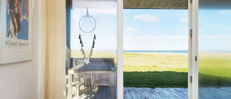 A room with a large sliding glass door leading to a deck with a view of the ocean.